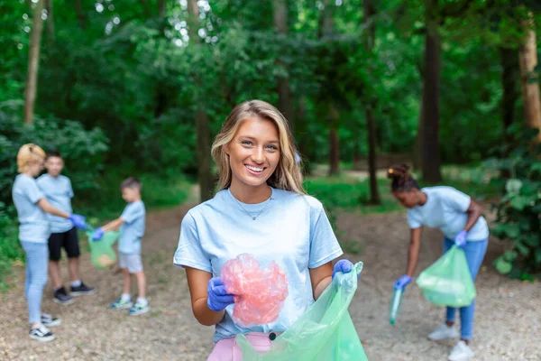 Young female volunteer cleaning the environment in the park, collecting litter in garbage bags.