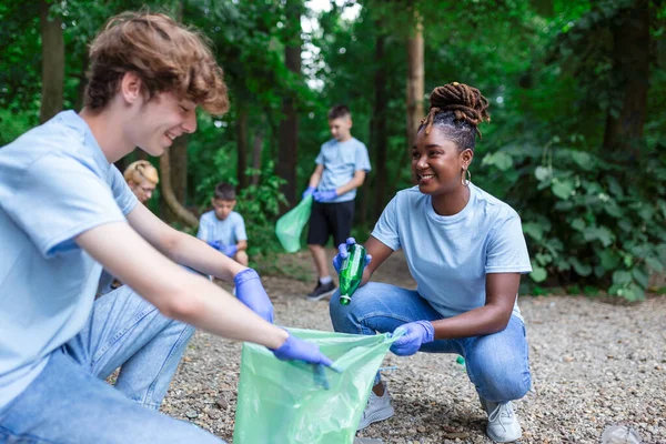 A group of people are cleaning together in a public park, protecting the environment. Woman in the foreground with a garbage bag in her hand cleans the park