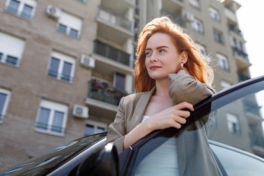 Sokakta arabanın yanında duran mutlu bir kadının portresi. Kapısı açık bir arabanın arkasında duran güzel beyaz bir kadın.