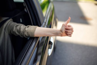 Ön planda bulanık araba kullanırken yan pencereden baş parmağını gösteren kadın görüntüsü