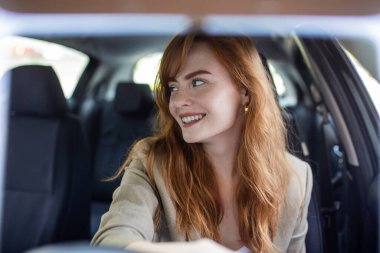 Gün batımında yeni arabasını süren güzel genç bir kadın. Arabadaki kadın. Hoş görünümlü güzel bir kadın portresi, mutlu bir yüz ifadesi, günlük giysili bir kadın araba sürüyor.