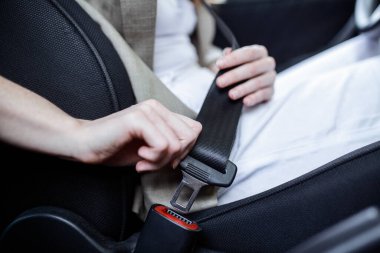 Ön planda bulanık bir şekilde arabada otururken emniyet kemerini takan kadın görüntüsü. Arabanın emniyet kemerini takan genç bir kadının ellerini kesin. Yalnız oturmak. Kapat.