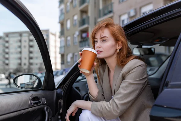 Happy young woman with coffee having a brake in her car. Side view of woman with coffee to go in hand. Young woman drinking coffee in her car
