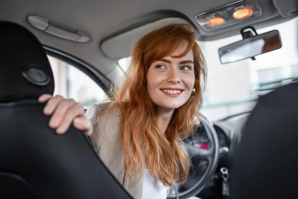 young woman looking back while driving car on blurred background. Back view of an attractive young business woman looking over her shoulder while driving a car