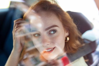 Kendinden emin ve güzel. Gündüz vakti araba sürerken gözlerini kaçıran, gündelik giysili çekici kızıl saçlı bir kadının ön görüntüsü. Gülümseyen güzel bir kadın araba kullanıyor, otomobilde oturuyor.