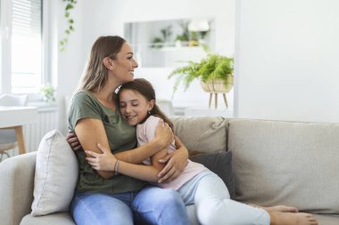 Tatlı güzel kızının genç annesine sarılıp yattığı yakın çekim. Sevgili anne, tatlı kızını evdeki kanepede kucaklıyor..