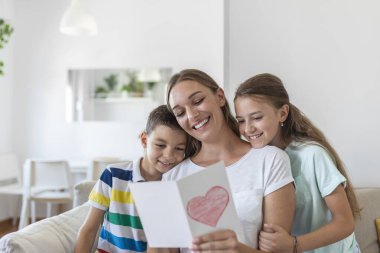 Mutlu küçük anne ve çocuklar kanepede oturup dileklerini okurken kucaklaşıyorlar ve evde sunulan kartpostalda tatille kutluyorlar.