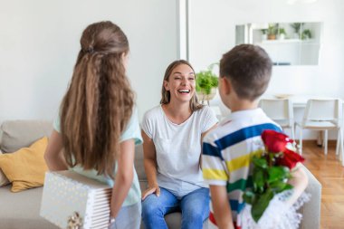 Mutlu çocuklar annelerine çiçek veriyorlar. Anneler Günün kutlu olsun! Çocuklar erkek ve kız gülümseyen anneyi kutlar, ona bir buket gül ve bayram kutlaması sırasında bir hediye kutusu verir.