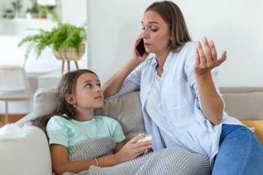 Anne hasta çocuğunun ateşini ölçüyor. Yüksek ateşi olan hasta bir çocuk yatakta yatıyor ve annesi termometreyi tutuyor. Cep telefonlu anne doktoru arıyor.