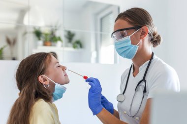 Hemşire küçük bir çocuğa burun temizleme testi yapıyor. COVID-19 salgınına bağlı PCR testinden geçen bir kız. PCR küçük kızı test ederken pamuk çubuğu kullanan kadın doktor.