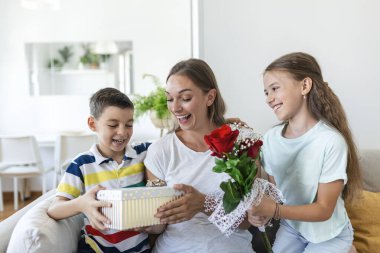Mutlu çocuklar annelerine çiçek veriyorlar. Anneler Günün kutlu olsun! Çocuklar erkek ve kız gülümseyen anneyi kutlar, ona bir buket gül ve bayram kutlaması sırasında bir hediye kutusu verir.