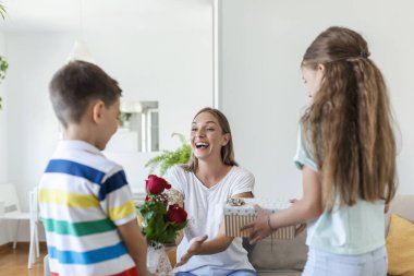 Hediye kutusu olan neşeli küçük bir kız ve gül buketi olan en küçük erkek kardeşi gülümseyerek anneler gününü evde kutluyor. Anneler Günün kutlu olsun.!