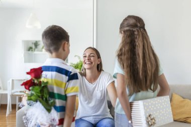 Mutlu çocuklar annelerine çiçek veriyorlar. Anneler Günün kutlu olsun! Çocuklar erkek ve kız gülümseyen anneyi kutlar, ona bir buket gül ve bayram kutlaması sırasında bir hediye kutusu verir.