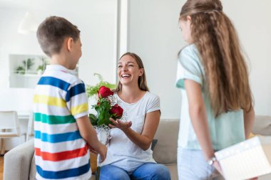 Mutlu çocuklar annelerine çiçek veriyorlar. Anneler Günün kutlu olsun! Çocuklar erkek ve kız gülümseyen anneyi kutlar, ona bir buket gül ve bayram kutlaması sırasında bir hediye kutusu verir.