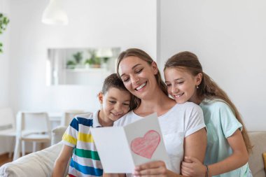Mutlu küçük anne ve çocuklar kanepede oturup dileklerini okurken kucaklaşıyorlar ve evde sunulan kartpostalda tatille kutluyorlar.