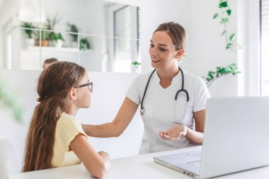Muayene odasında küçük bir kızla konsültasyon yapan bir doktor. 7 yaşındaki bayan hasta, doktorla muayenehanede konuşuyor.
