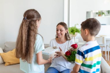Mutlu çocuklar annelerine çiçek veriyorlar. Anneler Günün kutlu olsun! Çocuklar erkek ve kız gülümseyen anneyi kutlar, ona bir buket gül ve bayram kutlaması sırasında bir hediye kutusu verir.