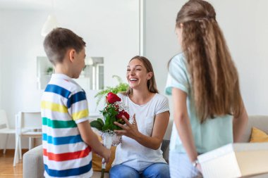 Mutlu çocuklar annelerine çiçek veriyorlar. Anneler Günün kutlu olsun! Çocuklar erkek ve kız gülümseyen anneyi kutlar, ona bir buket gül ve bayram kutlaması sırasında bir hediye kutusu verir.