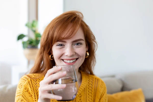Happy young woman smiling while holding a glass of water at home. Woman on living room sofa Relaxed and Smiling While Drinking glass of water. Health benefits of drinking enough water