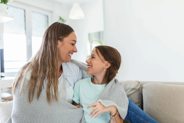 A nice girl and her mother enjoy sunny morning. Good time at home. Child wakes up from sleep. Family playing under blanket on the bed in the bedroom.