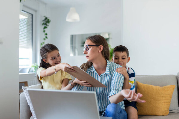 Woman working from home during quarantine with her little son and daughter on couch and screaming, demanding attention