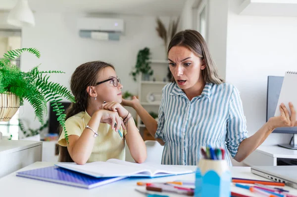 Stressed mother and daughter frustrated over failure homework, school problems concept. Sad little girl looking at mother, does not want to do boring homework