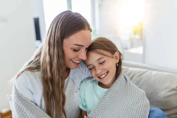 Caring young mother putting a coat on her daughter at home. Good time at home. Child wakes up from sleep. Family playing under blanket on the bed in the bedroom.