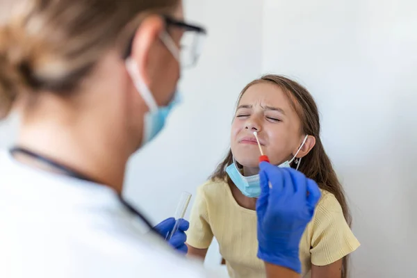 Nurse performing a nose swab test on a little child. Girl going through PCR testing due to COVID-19 pandemic. Female doctor using cotton swab while PCR testing small girl