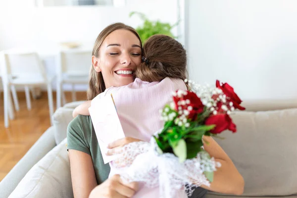 I love my you mom! Attractive young woman with little cute girl are spending time together at home, thanking for handmade card with love symbol and flowers. Happy family concept. Mother\'s day.