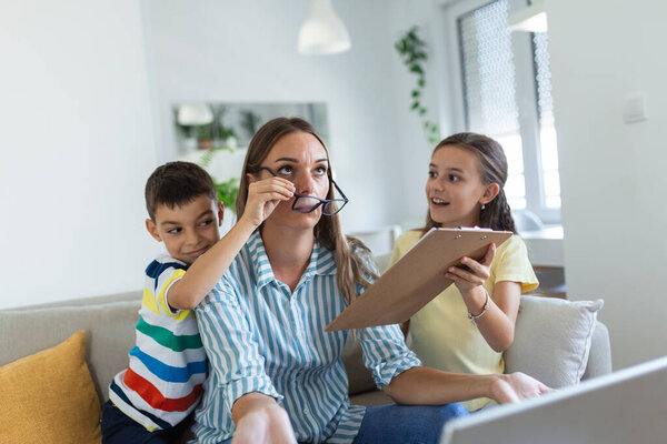 Upset mother having problem with noisy naughty daughter and son jumping on couch and screaming, demanding attention, frustrated mum tired of difficult child trying to work from home