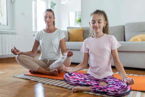 Yoga with kids. Young family mother and little daughter meditating with closed eyes while sitting in lotus pose on the flor in living room at home