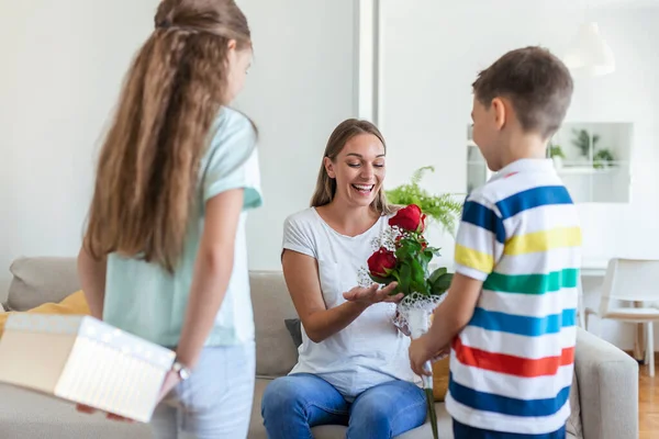 Mutlu çocuklar annelerine çiçek veriyorlar. Anneler Günün kutlu olsun! Çocuklar erkek ve kız gülümseyen anneyi kutlar, ona bir buket gül ve bayram kutlaması sırasında bir hediye kutusu verir.