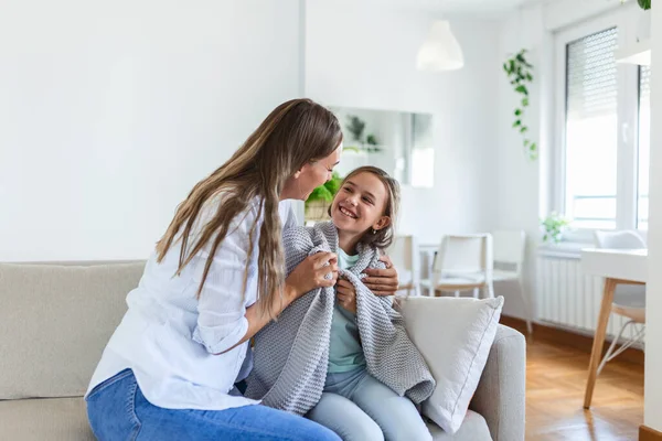 Caring young mother putting a coat on her daughter at home. Good time at home. Child wakes up from sleep. Family playing under blanket on the bed in the bedroom.