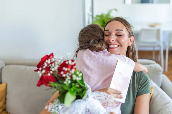 I love my you mom! Attractive young woman with little cute girl are spending time together at home, thanking for handmade card with love symbol and flowers. Happy family concept. Mother\'s day.