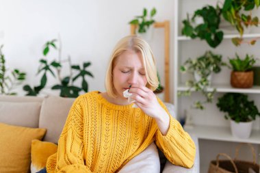 Hasta kadın. Flu. kadın üşüttü. Dokuların içine hapşırmak. Baş ağrısı. Virüs. İlaçlar. Mendile burnunu silen 19 numaralı kovansı enfekte genç kadın. Kanepede oturan, başı ağrıyan hasta kadın.