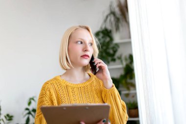 Cep telefonuyla konuşurken kağıt tutan düşünceli bir kadın. Dişi, pencereden bakıyor. O evde..