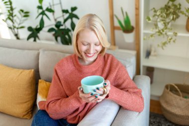 Beautiful young woman drinking tea at home. Looking away. Happy young woman meets morning with cup of coffee at window. Woman enjoying a cup of coffee in winter at home