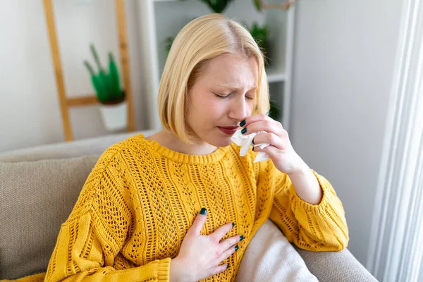 Sick Woman.Flu.Woman Caught Cold. Sneezing into Tissue. Headache. Virus .Medicines. Young Woman Infected With covid 19 Blowing Her Nose In Handkerchief. Sick woman with a headache sitting on a sofa