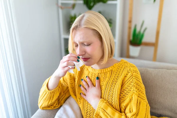 Sick Woman.Flu.Woman Caught Cold. Sneezing into Tissue. Headache. Virus .Medicines. Young Woman Infected With covid 19 Blowing Her Nose In Handkerchief. Sick woman with a headache sitting on a sofa