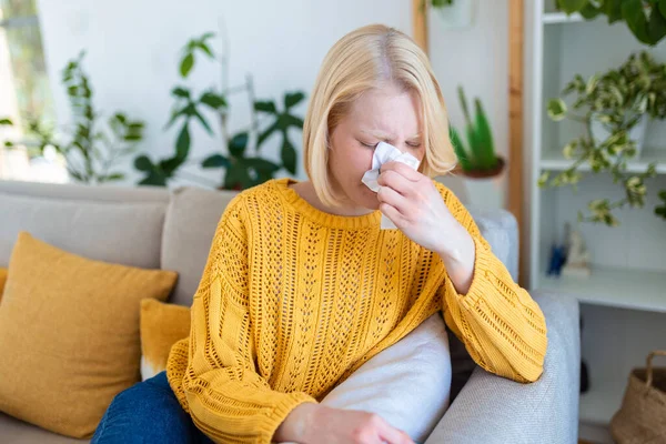 生病的女人 女人感冒了 在组织里打喷嚏头疼 年轻女人感染了鱼子酱19把她的鼻子吹在手巾上 一个头痛的生病女人坐在沙发上 — 图库照片