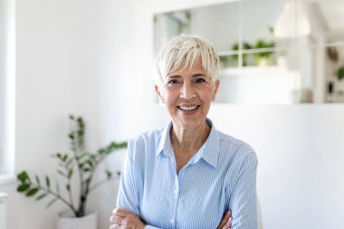 Kıdemli kadın kameraya bakıyor. Başarılı bir iş kadını. Gri saçlarıyla ofiste duran mutlu yaşlı profesör.