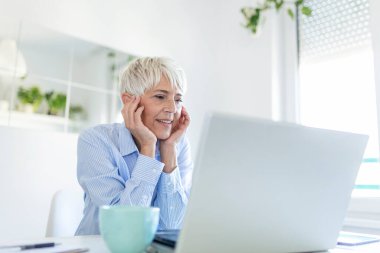 Portrait of casual woman using her laptop while sitting home office and working. An attractive middle aged businesswoman sitting in front of laptop and managing her small business from home.