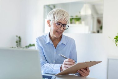 Elderly woman working on laptop computer, smiling. Woman Working From Home On Laptop In Modern Apartment. Trendy woman working on laptop from home