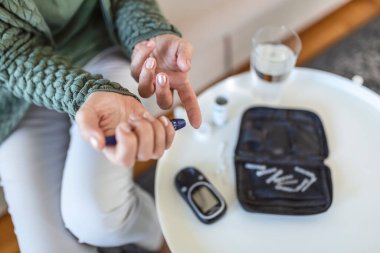 Glukometresi olan yaşlı kadında kan şekeri testi yapın. Parmakta şeker seviyesini ölçmeye hazır kırmızı bir kan damlası. Erkek parmağını kan damlası ve test şeridiyle kapat.