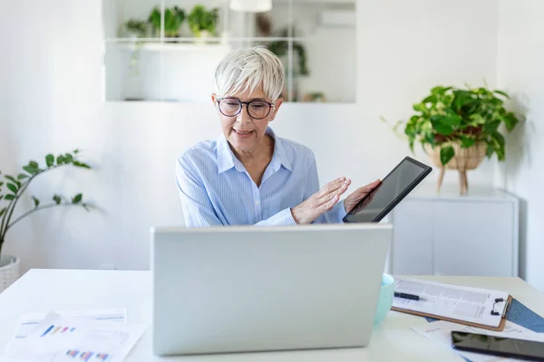 Focused businesswoman presenting charts and graphs on video call online. business, technology and people concept, Mature businesswoman with papers having video conference by laptop computer at office