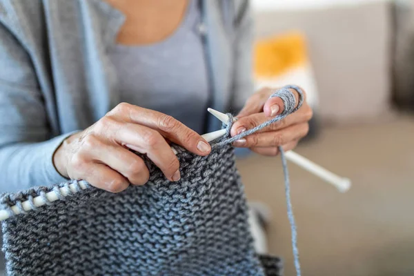 Close up view grandmother hands holding needles make repetitive motion knitting sitting on couch creating something with her arms. Hand knitting improve brain function, older generation hobby concept