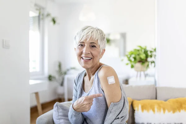 Woman pointing at her arm with a bandage after receiving the covid-19 vaccine. Mature woman showing her shoulder after getting coronavirus vaccine