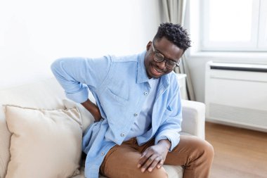 Mutsuz adam evde sırt ağrısı çekiyor. Bel Ağrısı. Adam sırt ağrısı hisseder masaj yapar kaslar ağrır, üzgün adam bel ağrısından muzdarip olur.