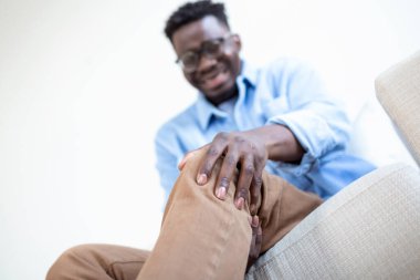 Evdeki oturma odasındaki koltukta oturan Afrikalı bir adamın fotoğrafı ve gün boyunca acıdan dizine dokunmak. Adam acılı dizine masaj yapıyor..