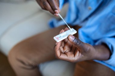 Genç Afrikalı Amerikalı adam evde antijen kiti ile COVID-19 testi yaptırıyor. Coronavirus enfeksiyonunu kontrol etmek için burun sopasıyla giriyoruz. Karantina, salgın hastalık.